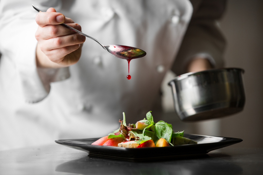 Chef drizzling sauce on plate and holding a pot