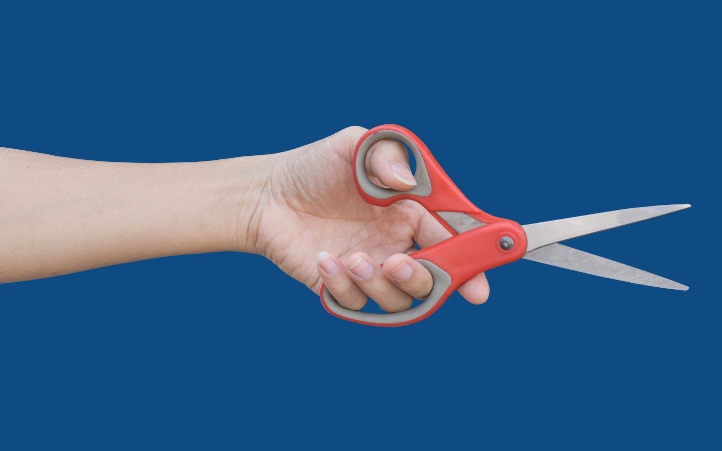 A hand with an open pair of scissors against a dark blue background