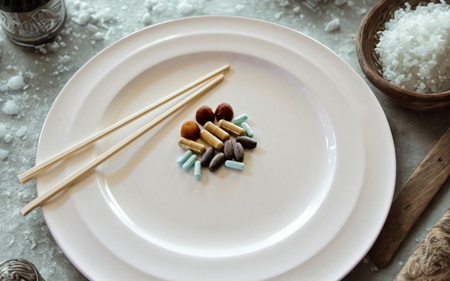 A white plate with various capsules of drugs in the centre with chopsticks on a table