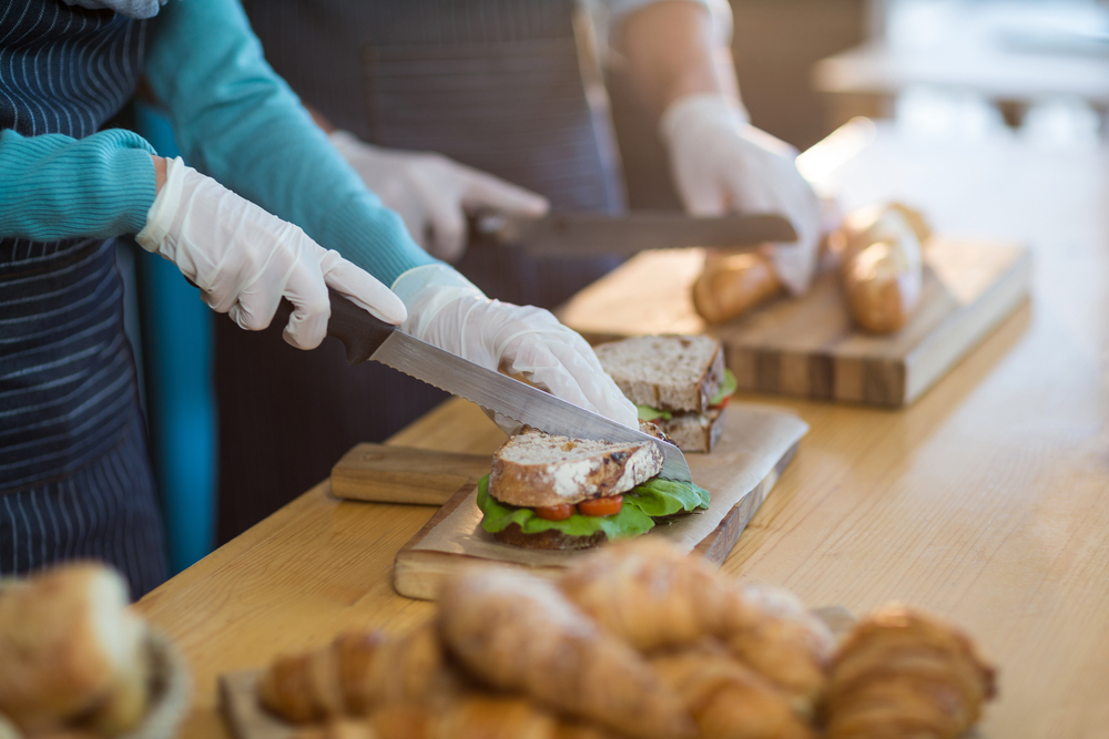 Mid-section of waiter chopping bread roll and sandwich on chopping board in cafe