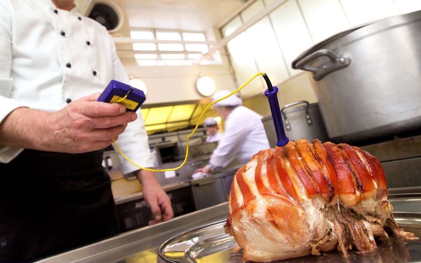 A chef with a temperature probe checking a pork roast is cooked through
